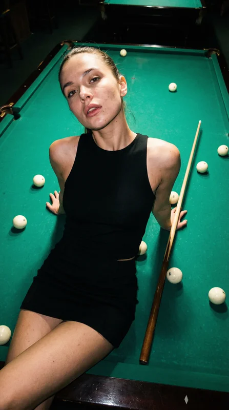 Woman in a black dress holding a cue beside a green billiards table
